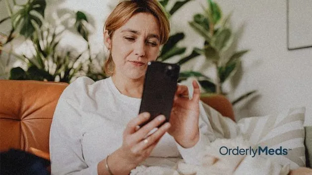 Woman sitting on a coach inside checking to see if she qualifies for GLP-1 treatment on her cell phone